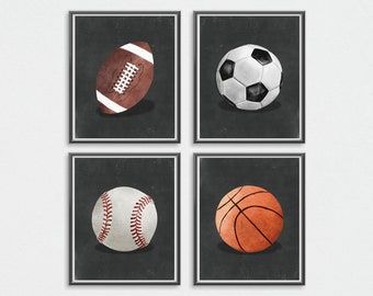 May include: Four black and white framed prints with a dark grey background. Each print features a different sport ball: a brown and white football, a black and white football, a white baseball with red stitching, and an orange basketball.