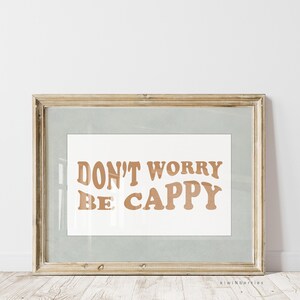 May include: A framed print with the text "DON'T WORRY BE CAPPY" in a brown font on a white background. The frame is a light wood colour.