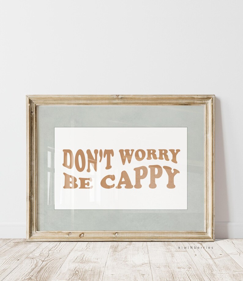 May include: A framed print with the text "DON'T WORRY BE CAPPY" in a brown font on a white background. The frame is a light wood colour.