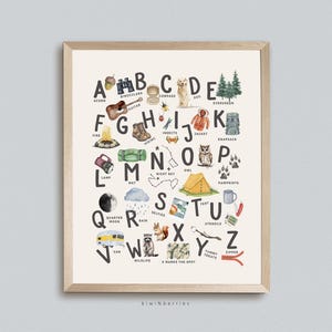 May include: A framed print featuring an illustrated alphabet with camping and outdoor-themed images. Each letter showcases a different item, such as an acorn, binoculars, a guitar, a compass, and a dog. The print is in a wooden frame.