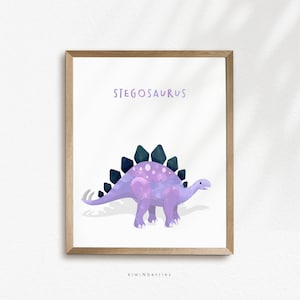 May include: A printable art print featuring a purple and blue cartoon Stegosaurus with the text "Stegosaurus" above the dinosaur. The print has a white background and is framed in a light brown frame. The text "kiwiNberries" is at the bottom of the print.
