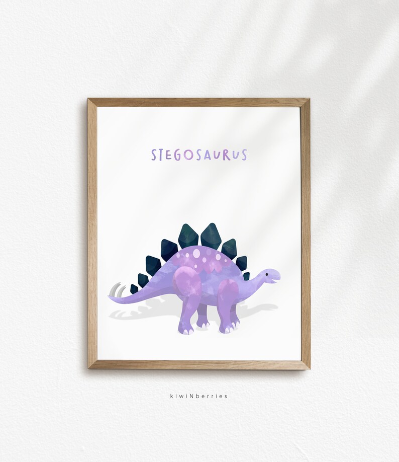 May include: A printable art print featuring a purple and blue cartoon Stegosaurus with the text "Stegosaurus" above the dinosaur. The print has a white background and is framed in a light brown frame. The text "kiwiNberries" is at the bottom of the print.