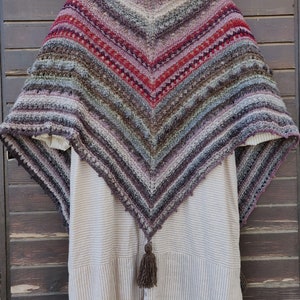 Könnte beinhalten: Ein dreieckiger Schal mit einem gehäkelten Muster in Braun-, Lila- und Rottönen. Der Schal hat einen Fransenrand und eine Quaste unten.