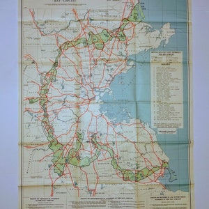 May include: A vintage map of the Bay Circuit, a network of public reservations in Massachusetts. The map shows the locations of various parks, forests, and other natural areas, as well as the roads and highways that intersect the circuit. The map is printed on a light blue background with red and green lines and text.