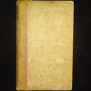 May include: A vintage book with a yellowed cover and a red spine. The book is worn and has a few stains.