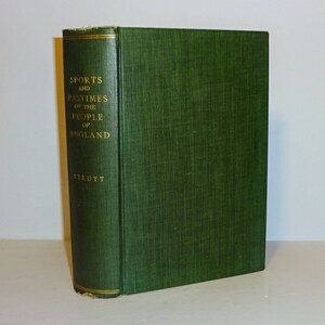 May include: A hardcover book titled "Sports and Pastimes of the People of England" by Strutt. The book has a dark green cover with gold lettering on the spine. The book is standing upright.