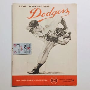 May include: Vintage Los Angeles Dodgers baseball program cover. The cover features an illustration of a baseball pitcher in action, with the team name in orange script. Includes a ticket stub and the text "Los Angeles Coliseum".