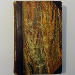 May include: A vintage book with a marbled cover in shades of brown, green, and yellow. The book has a dark brown spine and is bound in leather.
