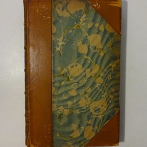 May include: A brown leather-bound book with a marbled paper cover. The marbling is in shades of green, brown, and white.