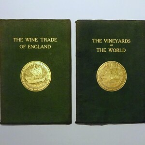 May include: Two green hardcover books with gold lettering and illustrations. The book on the left is titled "The Wine Trade of England" and the book on the right is titled "The Vineyards of the World".