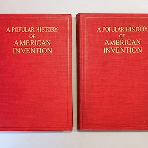 May include: Two red hardcover books with gold lettering. The text on the cover reads "A Popular History of American Invention". The books are side-by-side, with a textured surface.