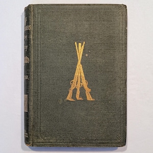 May include: Antique book with a dark green cover and gold embossed text and design. The cover features a gold illustration of crossed rifles. The book's spine has faded gold lettering. The book is slightly worn.