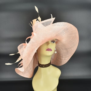 May include: A peach-coloured wide-brimmed hat with a ruffled design and feathers. The hat is on a mannequin head.