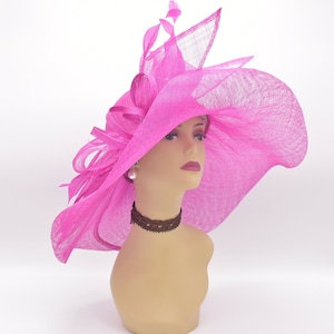 May include: A large, bright pink, wide-brimmed hat with a ruffled design and a small feather accent. The hat is made of a soft, lightweight material and is perfect for a special occasion.