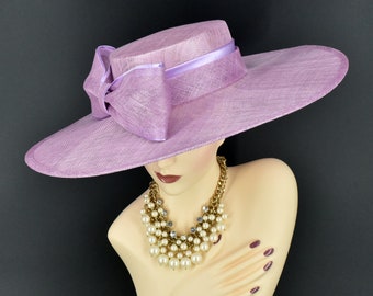May include: A wide-brimmed lilac hat with a matching satin ribbon bow. The hat is made of a straw-like material and has a slightly rounded crown.