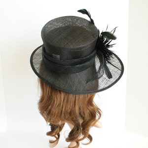 May include: A black hat with a wide brim and a black feather trim. The hat is made of a straw-like material.