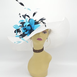 May include: A white wide-brimmed hat with a blue and black feather embellishment. The hat is made of a straw-like material and has a wide brim that curves down on the sides.