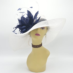May include: A white wide-brimmed hat with a navy blue feather embellishment. The hat is worn on a mannequin with a brown choker necklace.