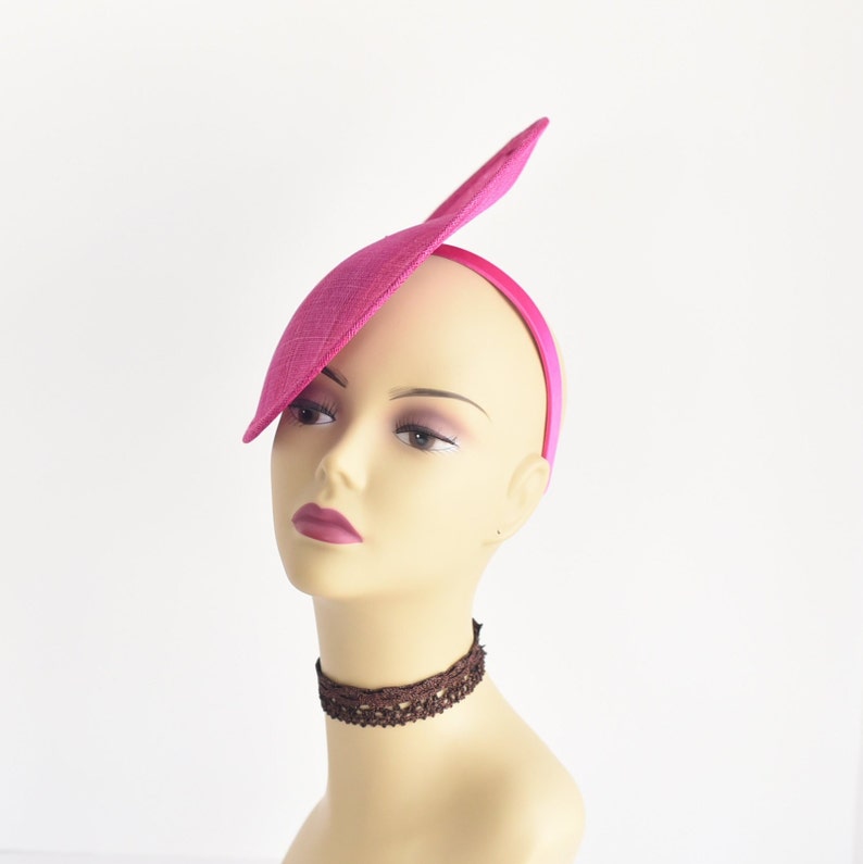 May include: A pink fabric hat with a single, long, pointed flap. The hat is worn on a mannequin's head.
