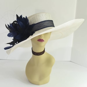 May include: A white wide-brimmed hat with a navy blue ribbon and a large navy blue feather accent.