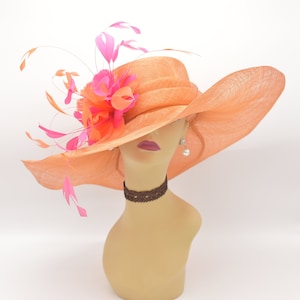 May include: A large, wide-brimmed hat in a peachy orange colour with a pink and orange flower accent and pink feathers.
