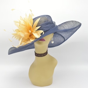 May include: A wide-brimmed navy blue hat with a large yellow flower accent. The hat is made of a straw-like material and has a wide brim that curves down on the sides. The flower is made of feathers and has a bright yellow colour.