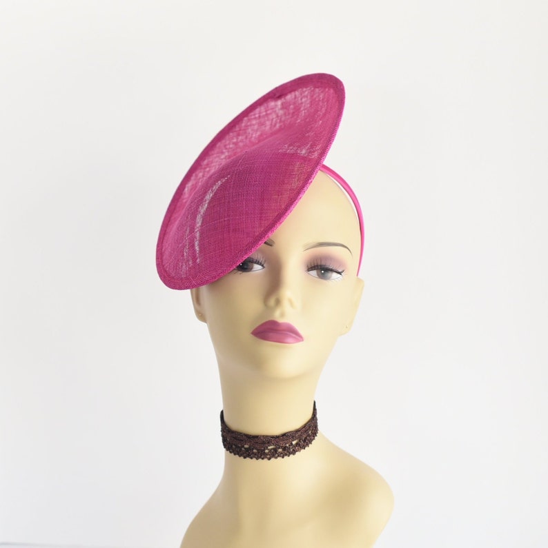May include: A bright pink, wide-brimmed hat with a slightly angled brim. The hat is made of a textured fabric and is worn on a mannequin.