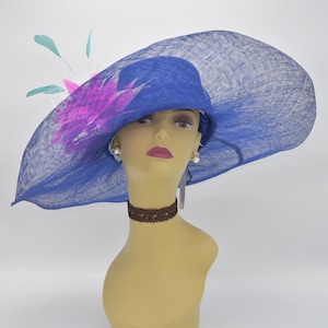 May include: A large blue hat with a wide brim and a pink and white feather accent. The hat is made of a woven material and has a slightly textured surface.