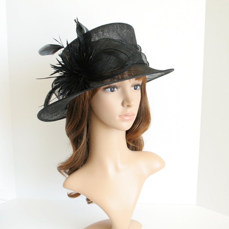 May include: A black hat with a wide brim and a black feather embellishment. The hat is made of a straw-like material.