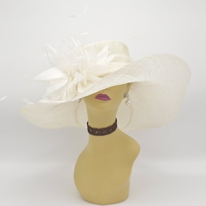 May include: A wide-brimmed ivory hat with a large white feather flower accent. The hat is on a mannequin head with a brown choker necklace.