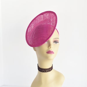 May include: A bright pink, round, wide-brimmed hat made of straw. The hat is tilted at an angle and is worn on a mannequin's head.