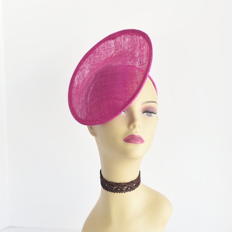 May include: A bright pink, round, wide-brimmed hat made of straw. The hat is tilted at an angle and is worn on a mannequin's head.