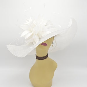 May include: A white wide-brimmed hat with a large white flower and feathers on the crown. The hat is on a mannequin head.