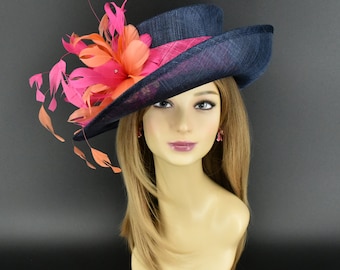 Puede incluir: Un sombrero azul marino con ala ancha, con un arreglo floral rosa y naranja con plumas. El sombrero tiene una banda rosa y se muestra en una cabeza de maniquí.