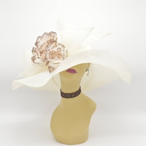 May include: A white wide-brimmed hat with a brown flower embellishment. The hat is on a mannequin head.