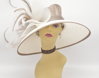 May include: A wide-brimmed hat with a brown and white color scheme. The hat has a large white bow and a brown feather accent. The hat is sitting on a mannequin head.