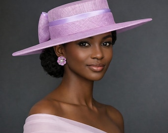 May include: A lavender wide-brimmed hat with a textured finish, featuring a matching satin ribbon band and a large side bow. The hat is paired with a lavender off-the-shoulder garment and a flower-shaped earring with a central pearl accent.