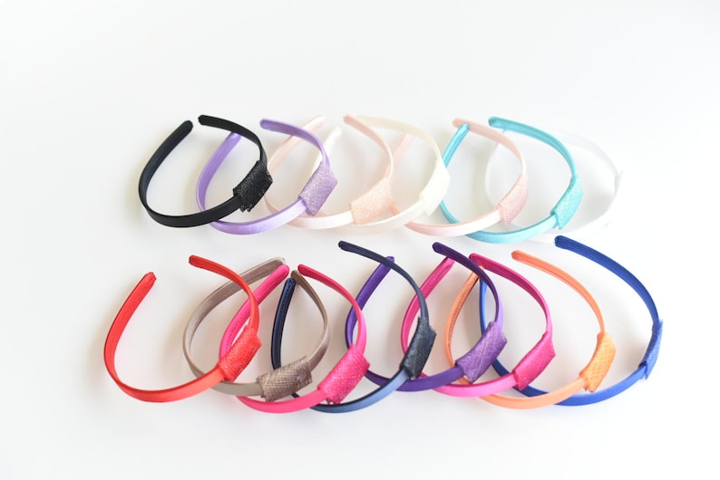May include: A set of 14 colorful satin headbands with a bow detail. The headbands are arranged in a semi-circle on a white background.
