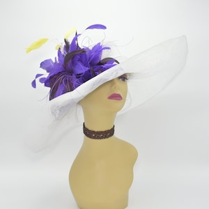 May include: A white wide-brimmed hat with a purple and yellow feather embellishment. The hat is made of a delicate, sheer material and has a wide brim that curves down on the sides.