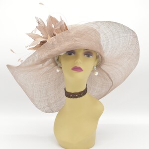 May include: A wide-brimmed hat made of beige straw with a large feather accent. The hat is worn on a mannequin with a brown choker necklace and pearl earrings.