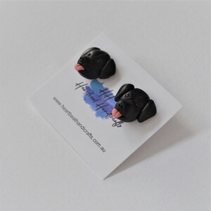 K&ouml;nnte beinhalten: Zwei schwarze Hunde-Ohrstecker mit rosa Zungen, pr&auml;sentiert auf einer wei&szlig;en Karte. Die Karte hat ein blaues Aquarelldesign und den Text "heartbeathandicrafts.com.au".