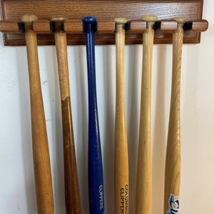 May include: A wooden wall-mounted baseball bat rack with six bats hanging on it. The bats are all wooden except for one blue bat with the word "Clippers" on it. Two of the bats have the words "Columbus Clippers" on them.