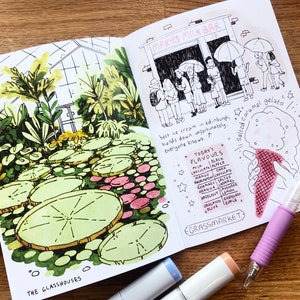 Puede incluir: Un cuaderno de bocetos abierto con una ilustraci&oacute;n dibujada a mano de un invernadero con hojas grandes y redondas y un cartel que dice "The Glasshouses". La p&aacute;gina derecha presenta un dibujo de una tienda llamada "Mary's Milk Bar" con una fila de personas esperando afuera. La p&aacute;gina tambi&eacute;n incluye una lista de sabores de helado y un dibujo de una mano sosteniendo un cono de helado de caramelo salado.