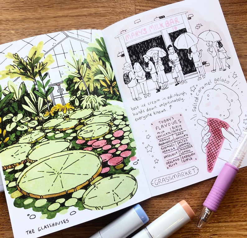 Puede incluir: Un cuaderno de bocetos abierto con una ilustraci&oacute;n dibujada a mano de un invernadero con hojas grandes y redondas y un cartel que dice "The Glasshouses". La p&aacute;gina derecha presenta un dibujo de una tienda llamada "Mary's Milk Bar" con una fila de personas esperando afuera. La p&aacute;gina tambi&eacute;n incluye una lista de sabores de helado y un dibujo de una mano sosteniendo un cono de helado de caramelo salado.