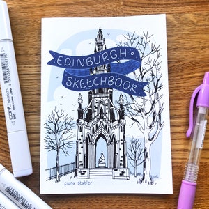 Puede incluir: Una portada de cuaderno de bocetos con una ilustraci&oacute;n dibujada a mano de un edificio con una torre y una pancarta que dice "EDINBURGH. SKETCHBOOK". La ilustraci&oacute;n est&aacute; en tinta negra sobre un fondo blanco con acentos azules.