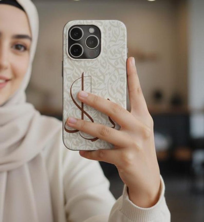 May include: A smartphone case featuring a light beige background with a subtle, repeating off-white calligraphic pattern. A prominent, dark brown stylized letter S is printed in the center of the case, which has a triple-lens camera cutout.
