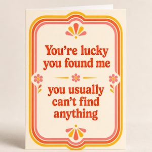May include: A cream-colored greeting card featuring a decorative border in shades of orange, pink, and yellow. The text reads, "You're lucky you found me you usually can't find anything," accented by small floral and fan-shaped graphic illustrations.