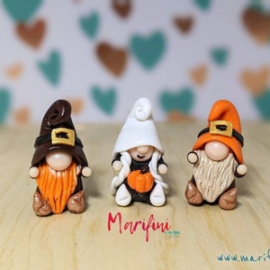May include: Three handmade gnome figurines with autumn-themed outfits. The gnomes are wearing brown, white and orange hats with gold accents. The gnome on the left has a brown hat and orange beard, the gnome in the middle has a white hat and a white beard, and the gnome on the right has an orange hat and a white beard.