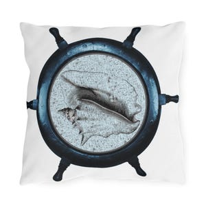 Może przedstawiać: Kwadratowa biała poduszka z granatowym wzorem koła sterowego. Środek koła ma jasnoniebieskie tło ze szczegółową ilustracją muszli. Poduszka ma motyw marynistyczny.