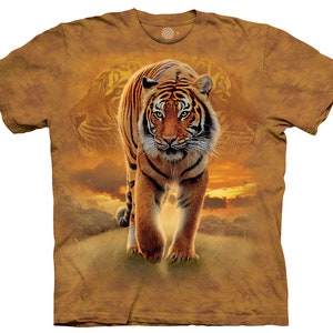 May include: A brown t-shirt with a tie-dye pattern featuring a tiger walking towards the viewer. The background is a sunset with clouds and a silhouette of trees.